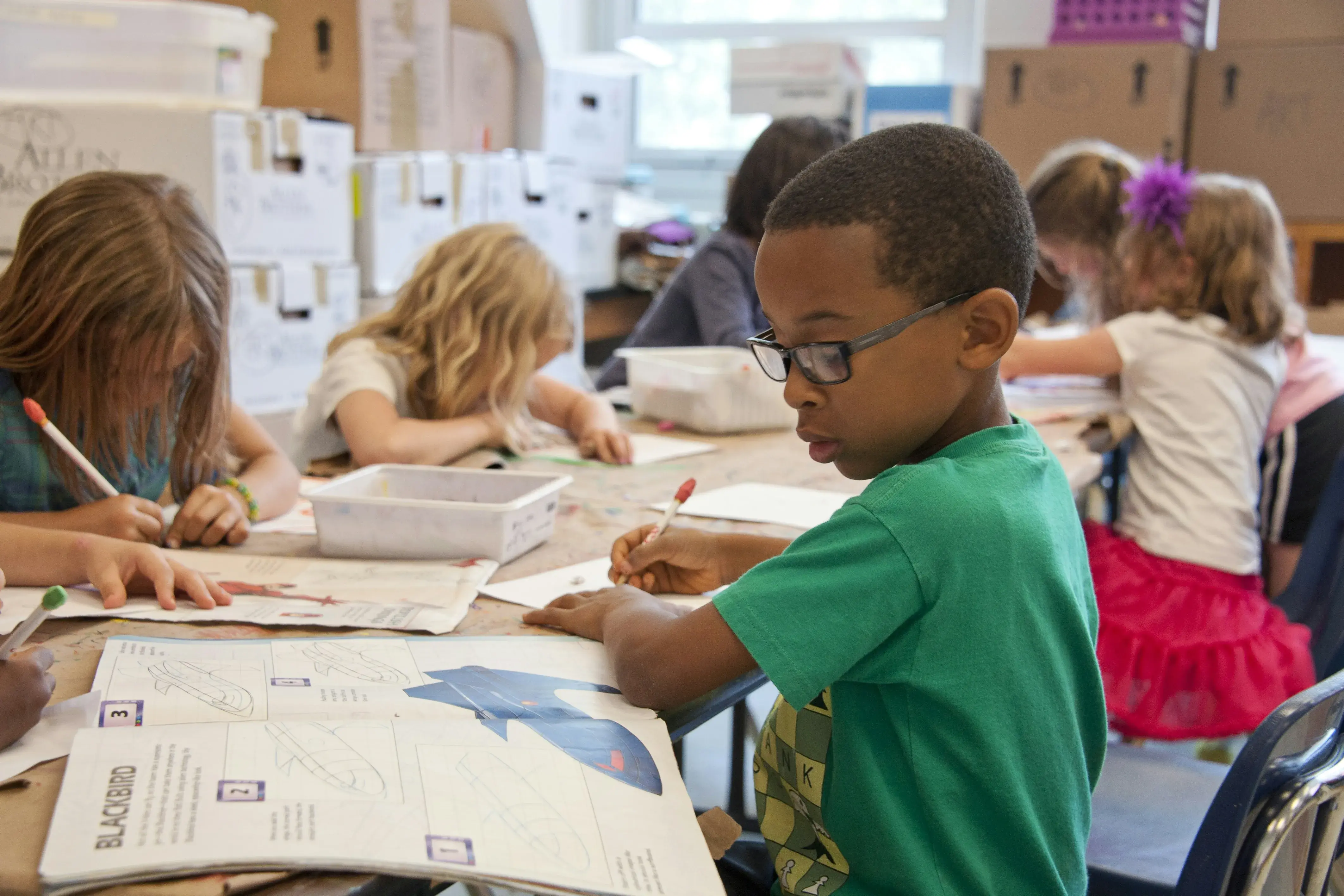 Several young kids sit at desks with books open