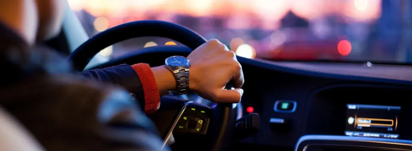 Person with a hand on the steering wheel of a car.